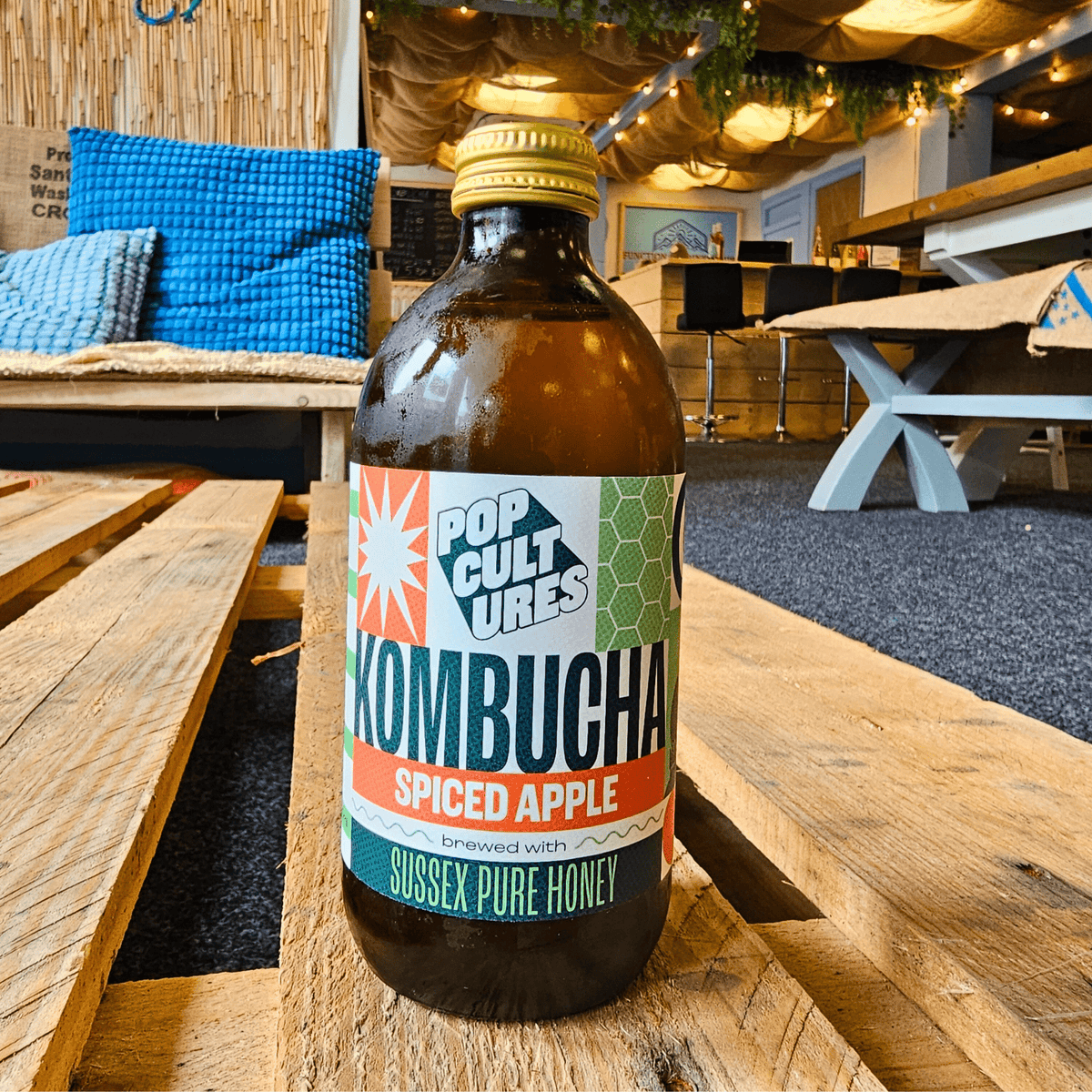 A bottle of Pop Cultures Apple & Cardamom raw jun kombucha on a wooden pallet table in the Otley taproom.