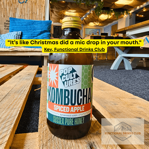 Pop Cultures Apple & Cardamom raw jun kombucha on a wooden pallet table in the Otley taproom, with Kev's tasting note: "It's like Christmas did a mic drop in your mouth."
