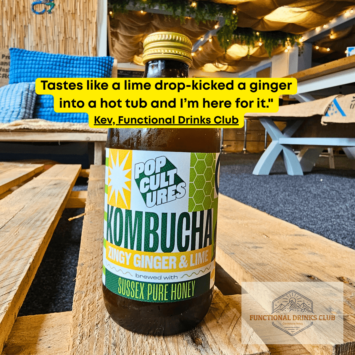 Pop Cultures Zingy Ginger & Lime raw jun kombucha on a wooden pallet table in the Otley taproom, with Kev's tasting note: "Tastes like a lime drop-kicked a ginger into a hot tub and I'm here for it."