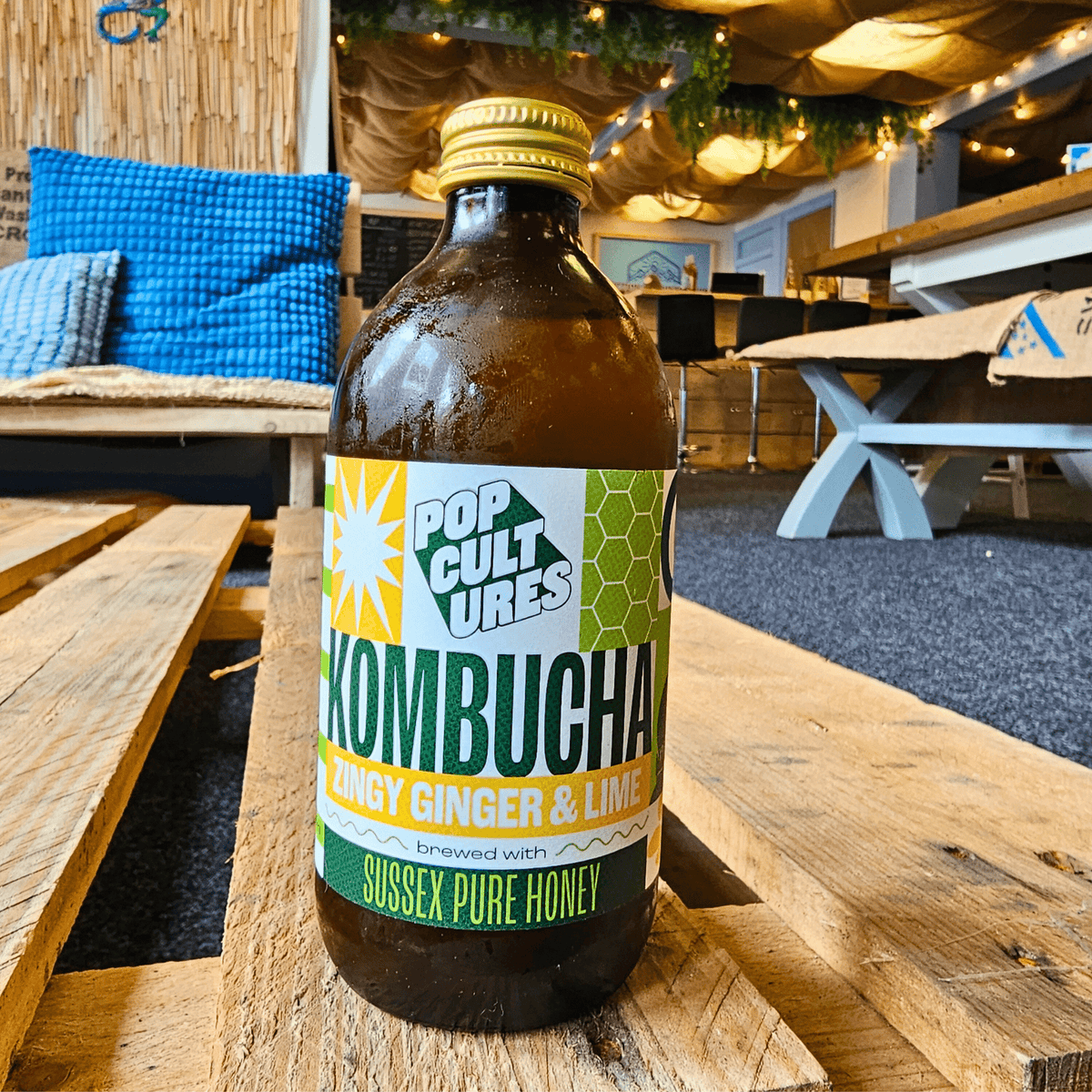 A bottle of Pop Cultures Zingy Ginger & Lime raw jun kombucha on a wooden pallet table in the Otley taproom.