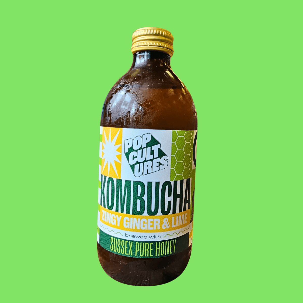 A bottle of Pop Cultures Zingy Ginger & Lime raw jun kombucha on a bright green background.
