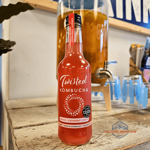 A bottle of Twisted Strawberry, Hibiscus & Ginger raw kombucha on a rustic wooden counter in the Otley taproom, with a glass kombucha dispenser behind.