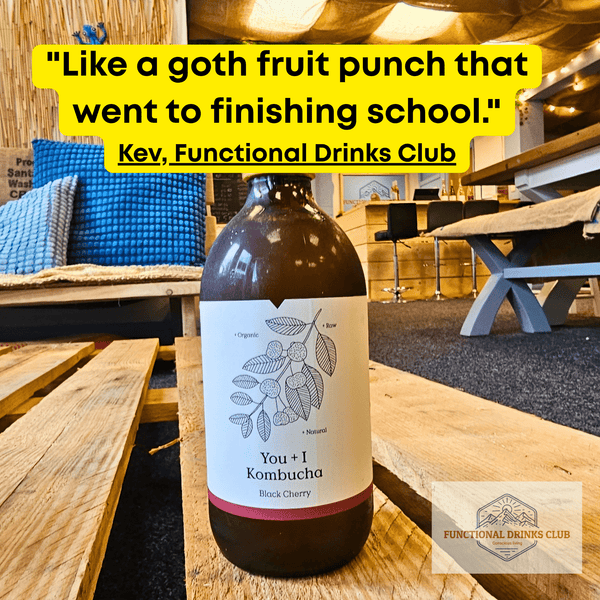 You + I Black Cherry raw kombucha on a wooden pallet table in the Otley taproom, with Kev's tasting note: "Like a goth fruit punch that went to finishing school."