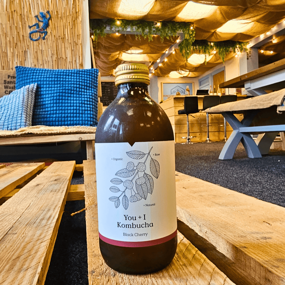 A bottle of You + I Black Cherry raw kombucha on a wooden pallet table in the Otley taproom.