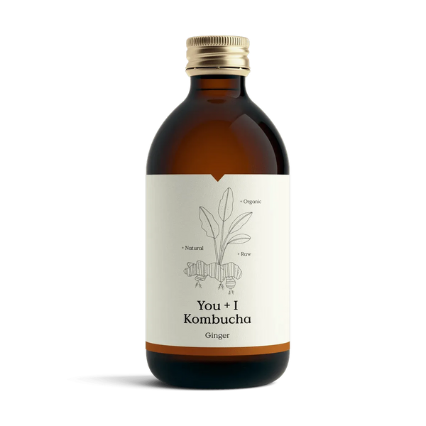 You + I Ginger raw kombucha in an amber glass bottle with a gold cap and a cream label with a botanical line drawing and an orange band.