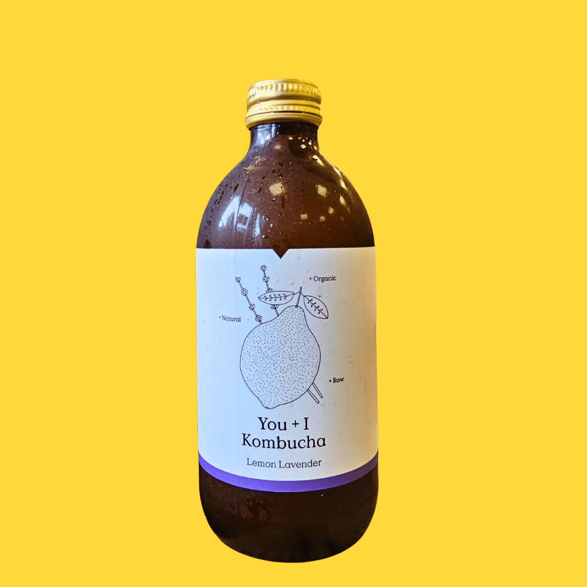 A bottle of You + I Lemon & Lavender raw kombucha on a bright yellow background.