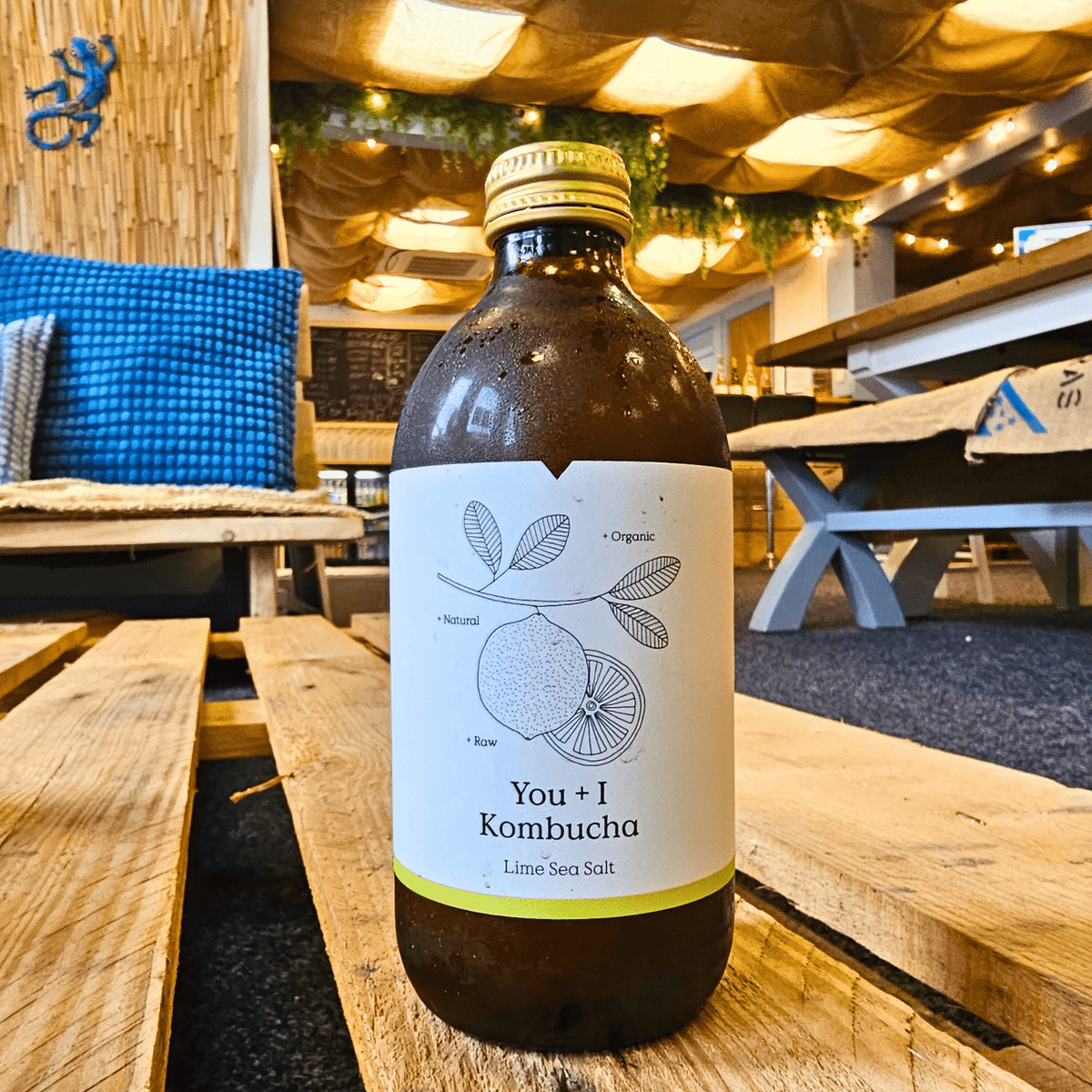A bottle of You + I Lime & Sea Salt raw kombucha on a wooden pallet table in the Otley taproom.