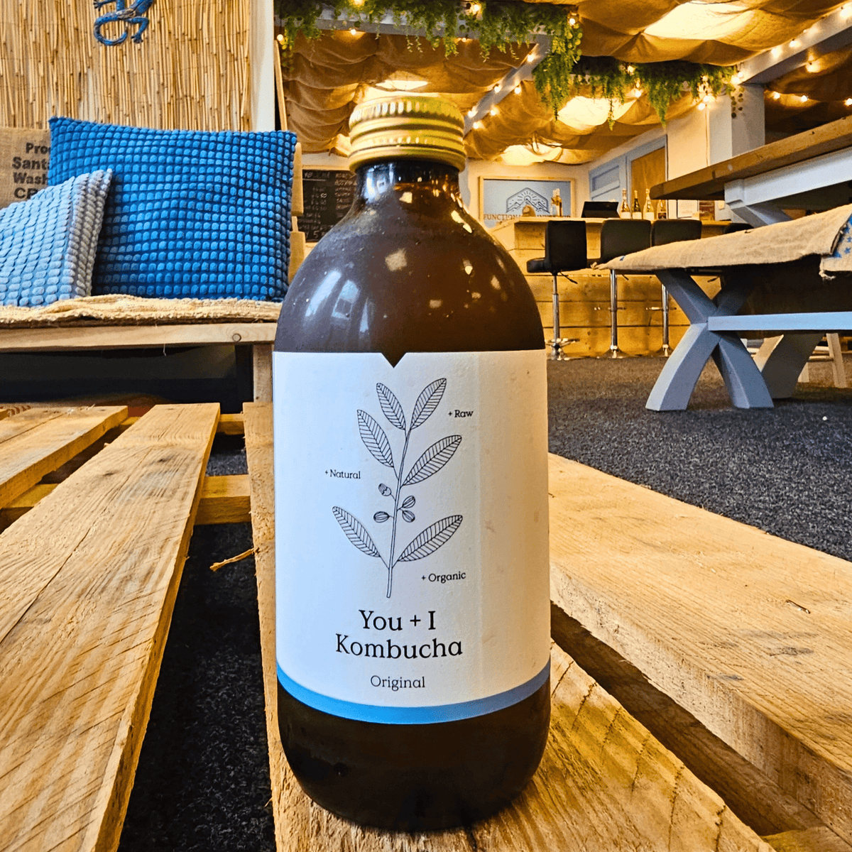 A bottle of You + I Original raw kombucha on a wooden pallet table in the Otley taproom.