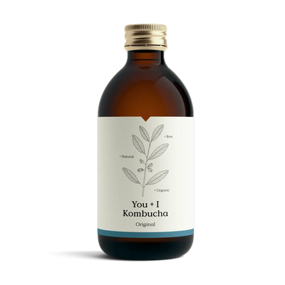 You + I Original raw kombucha in an amber glass bottle with a gold cap and a cream label with a botanical line drawing and a blue band.