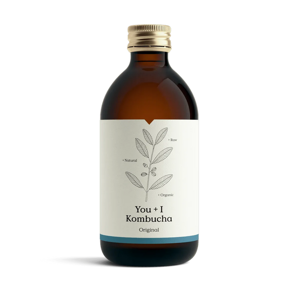 You + I Original raw kombucha in an amber glass bottle with a gold cap and a cream label with a botanical line drawing and a blue band.